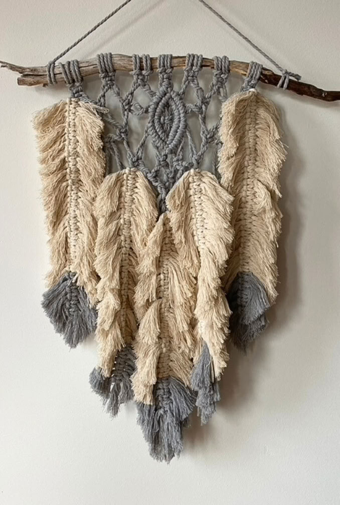 Beautifully crafted boho feather arrangement hanging vertical from a weathered branch