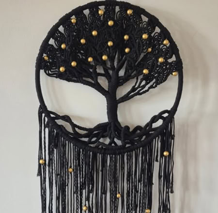 A black dreamcatcher with a tree design and gold beads, featuring long hanging tassels.